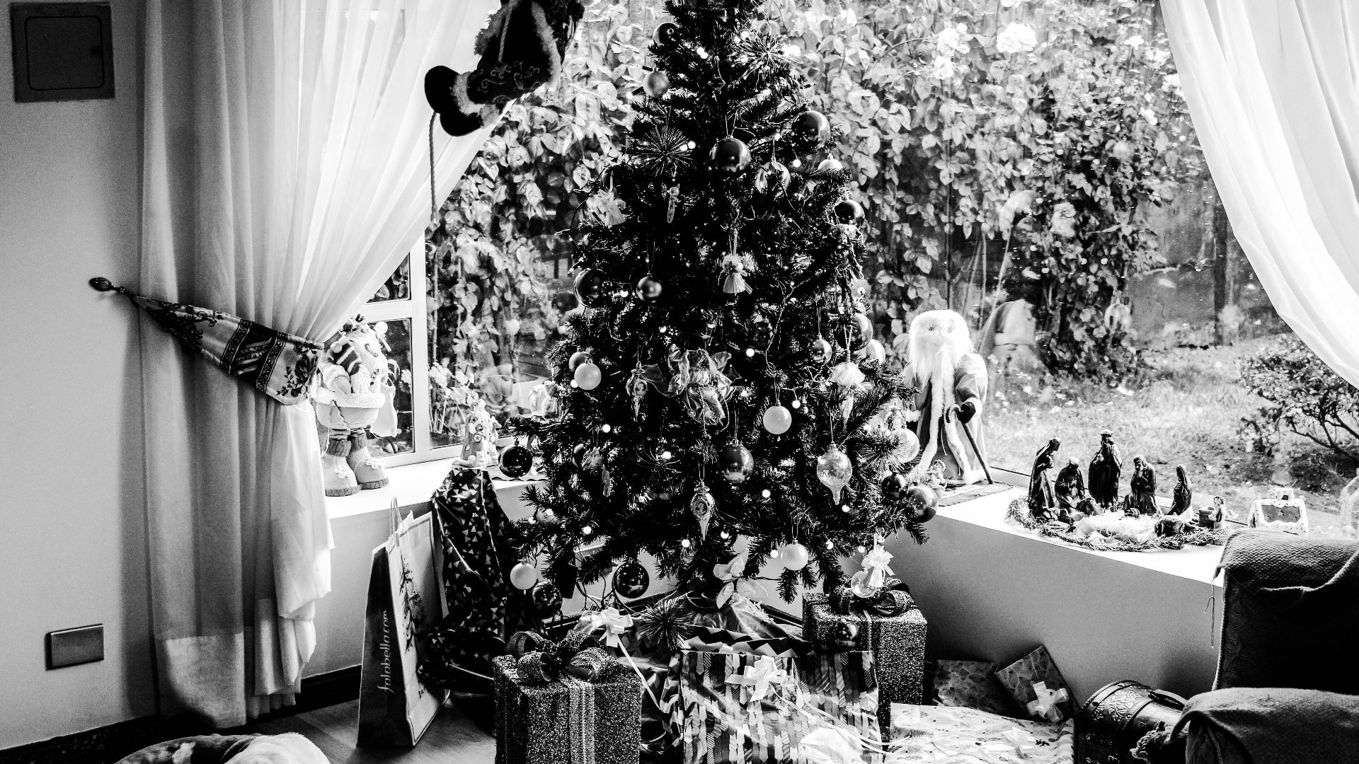 Cozy black and white photo of a decorated Christmas tree with gifts indoors.