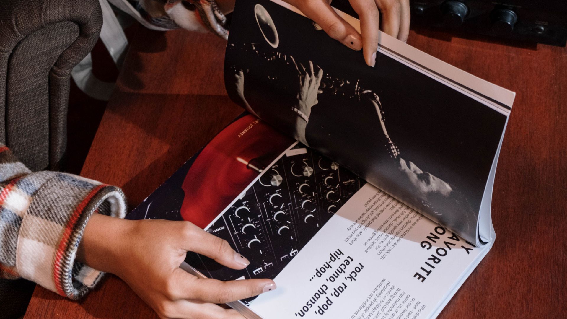 A person reads a music magazine near a vintage vinyl turntable indoors.
