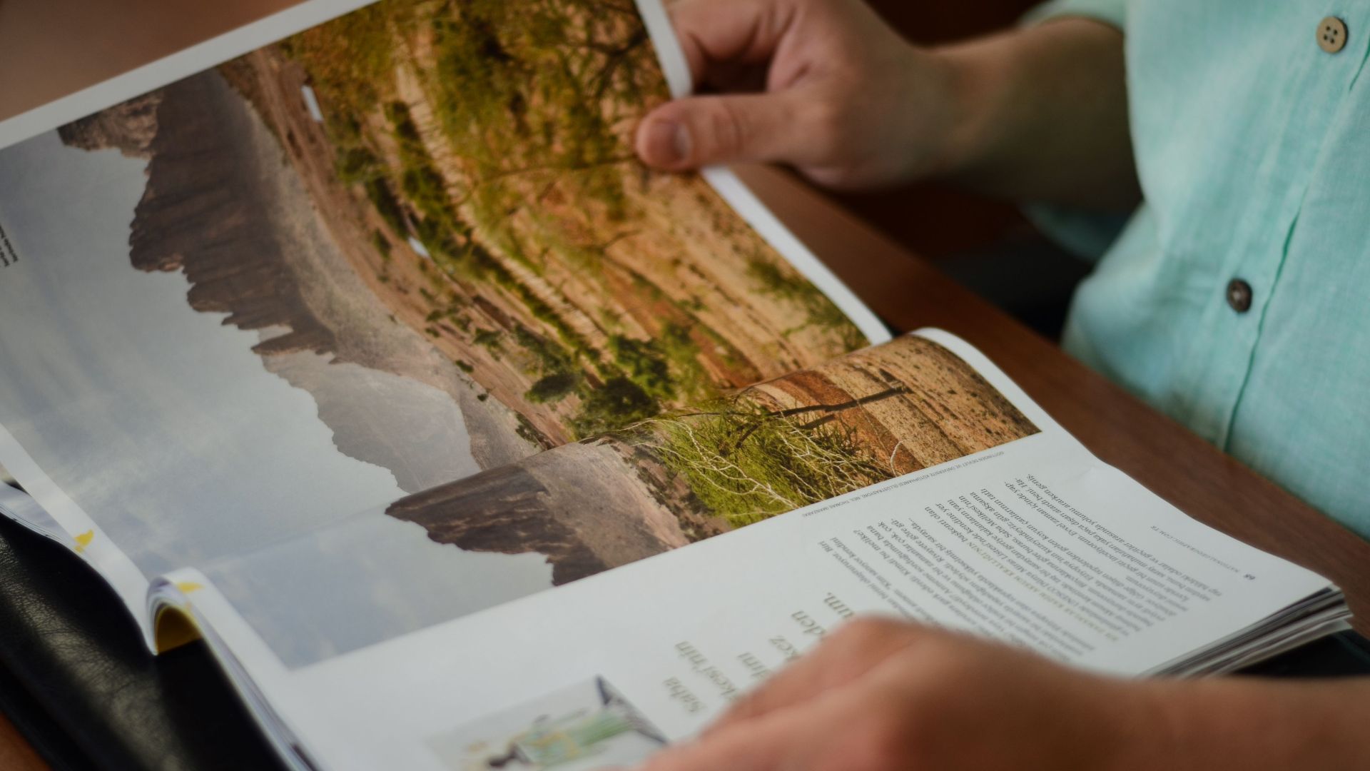 Close-up of a man reading a magazine indoors, focusing on hands and pages.