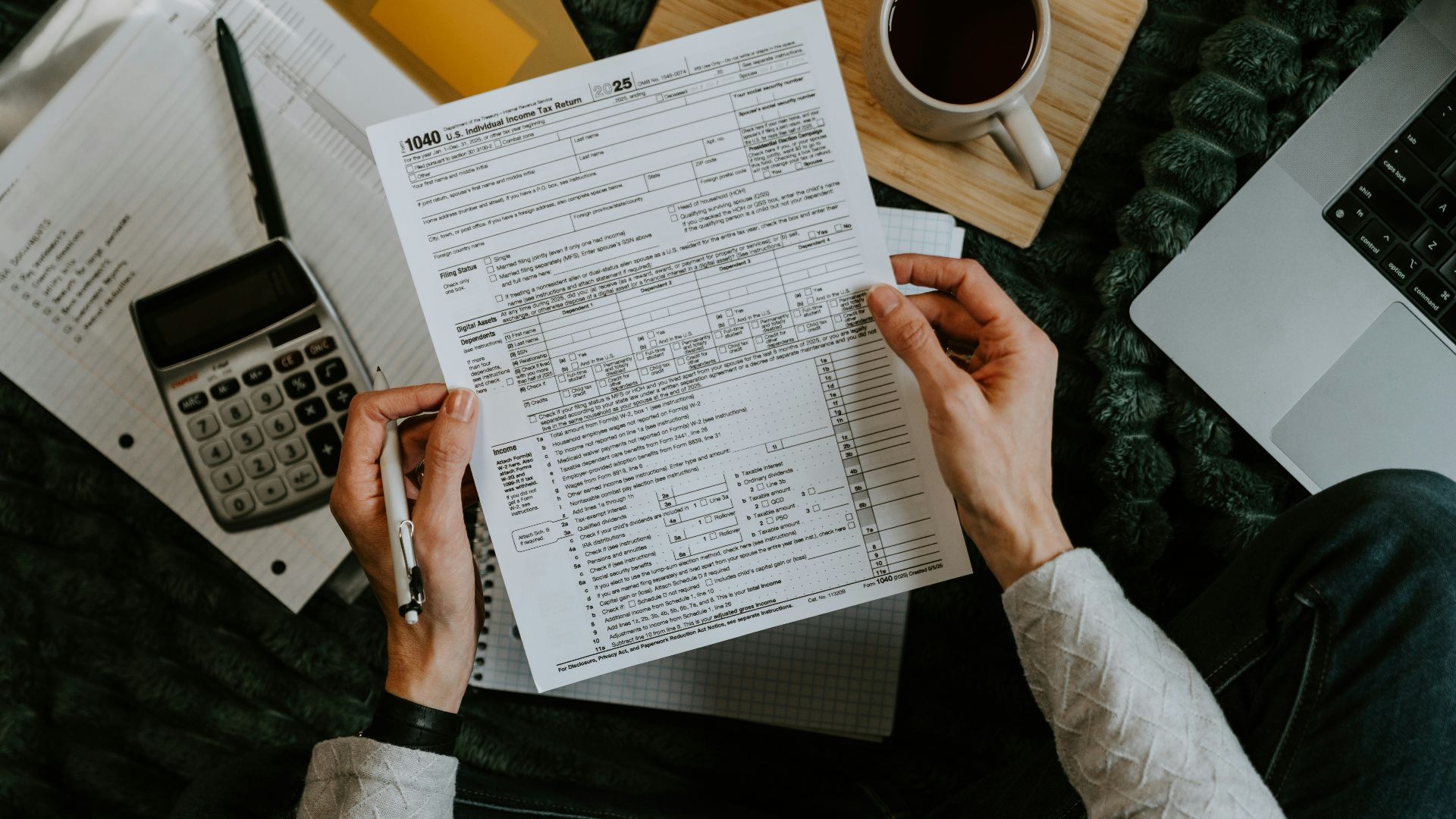 Hands holding tax forms with calculator and laptop