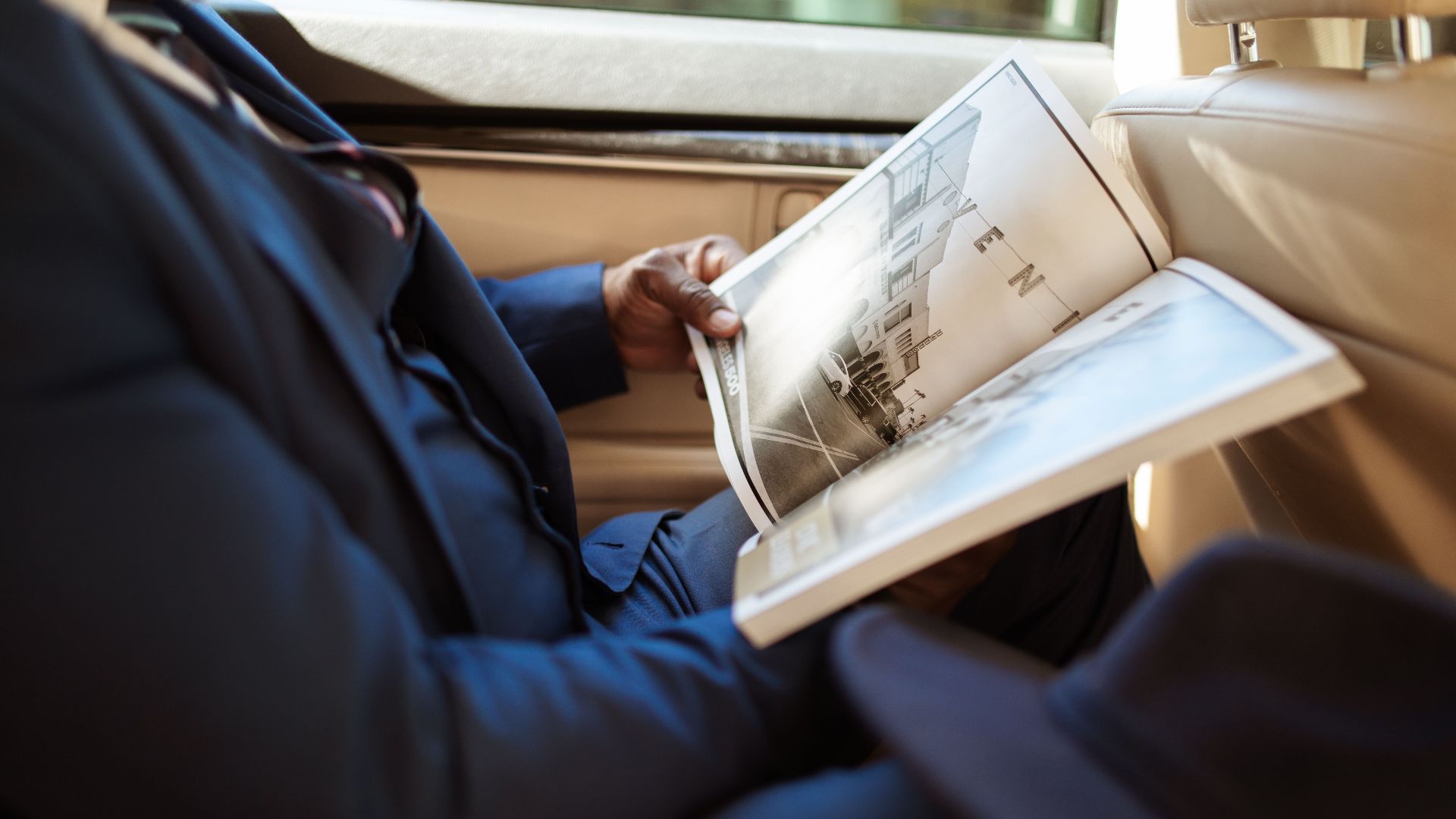 A businessman reads an open book while sitting in the backseat of a car.