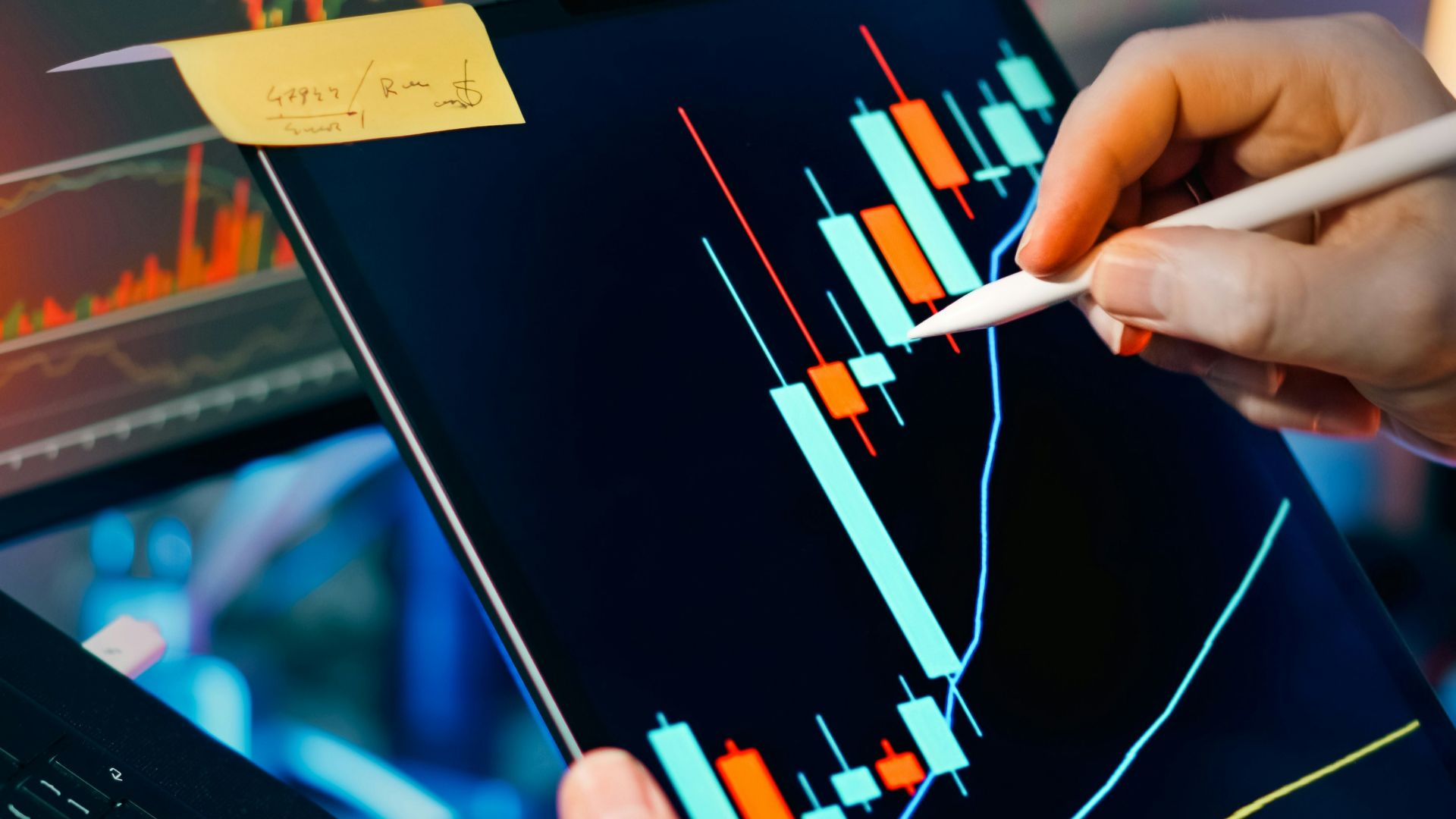 Trader analyzing stock market charts on tablet and monitor