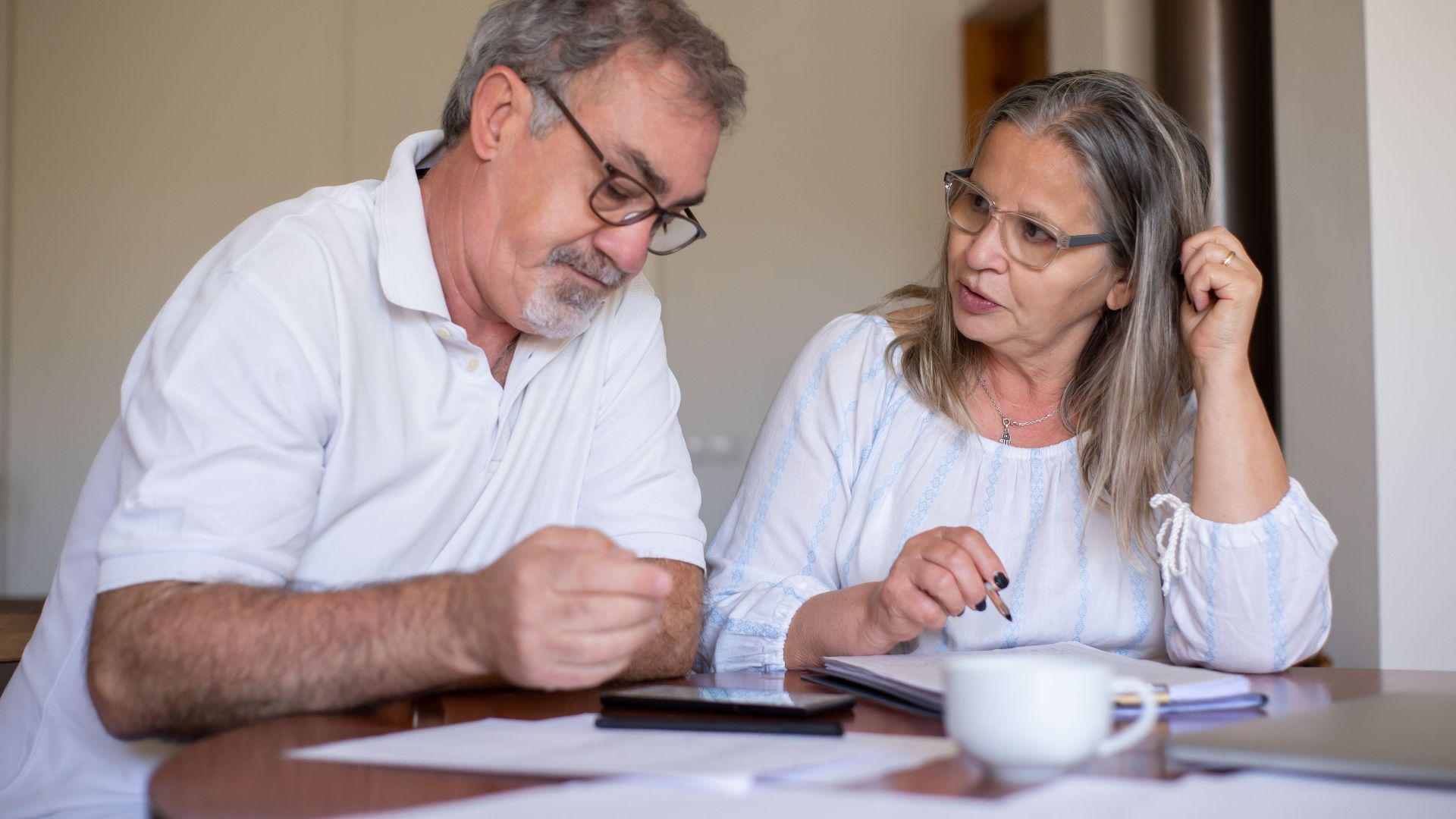Senior couple reviewing documents and managing finances together at home, showing collaboration and care.