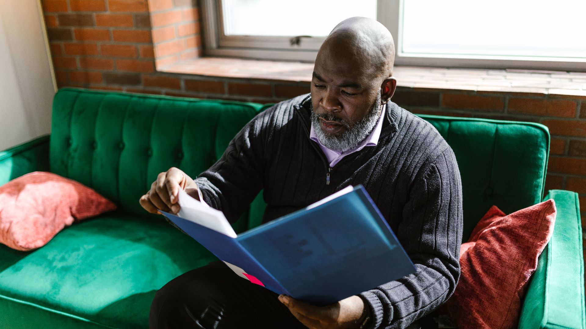 African American adult man reviewing documents on a green sofa, indoors.