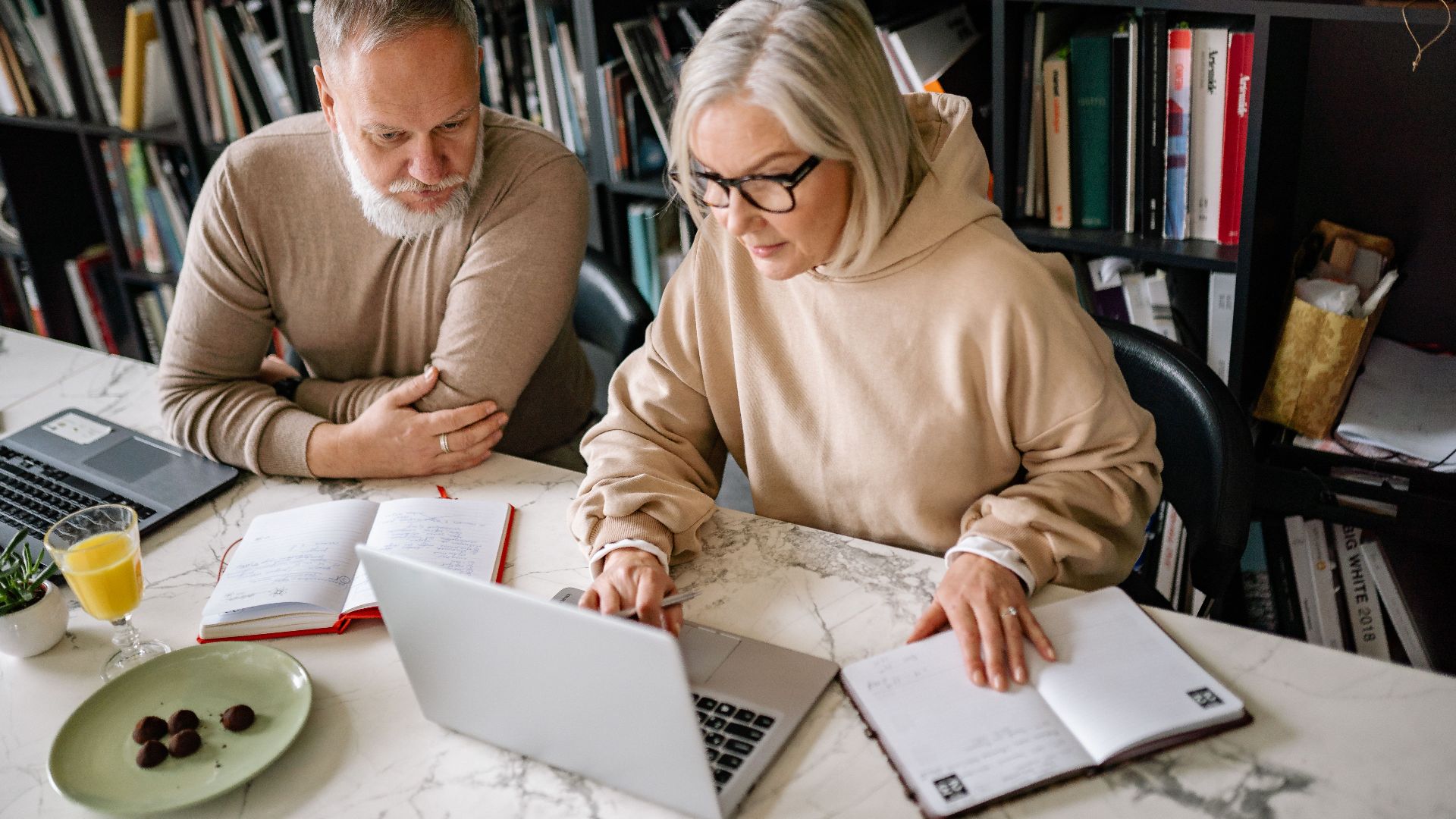 Elderly couple collaborating on laptops in a cozy home office setting.