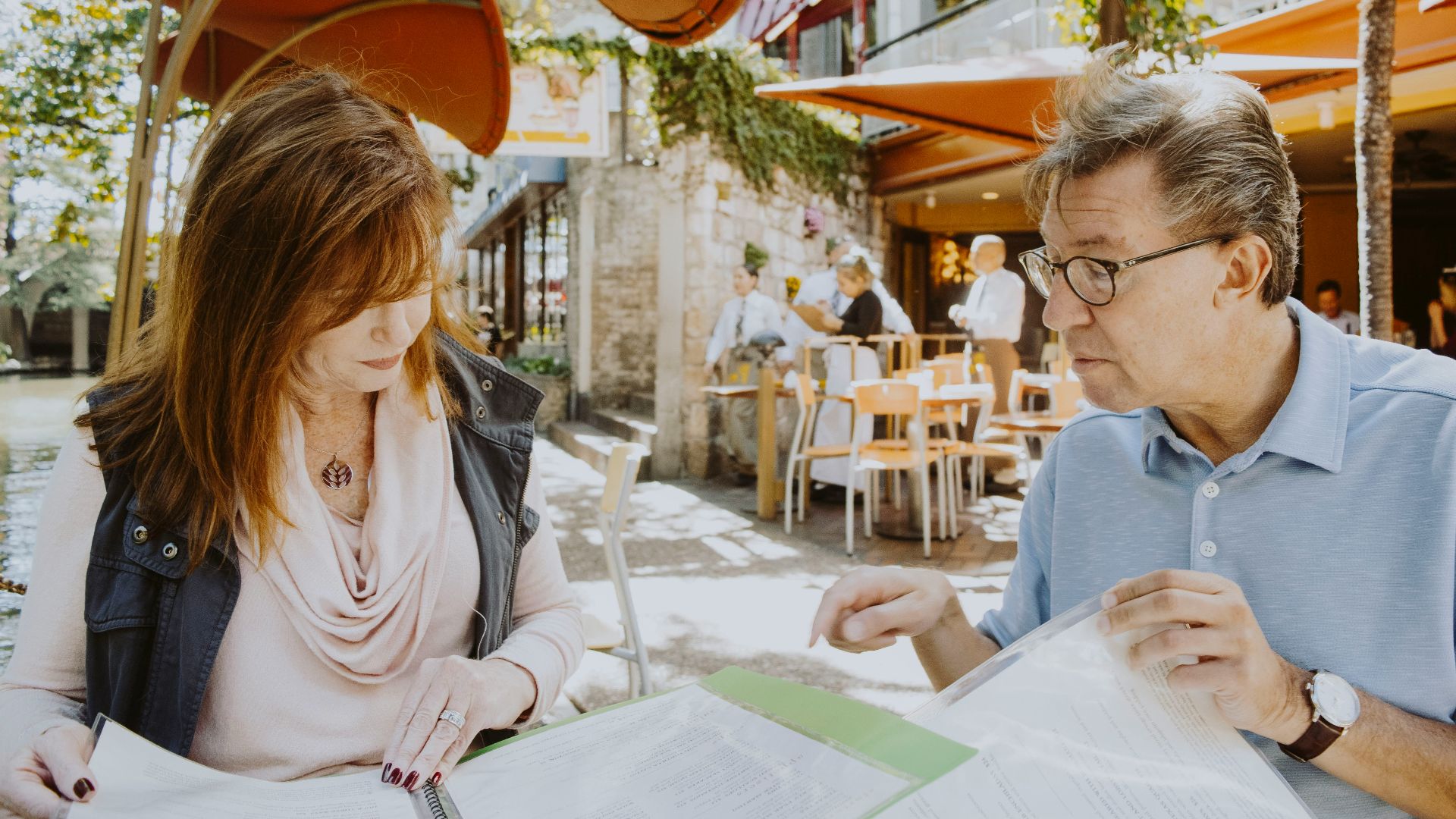 man and woman sitting down near table while reading outside cafe during daytime