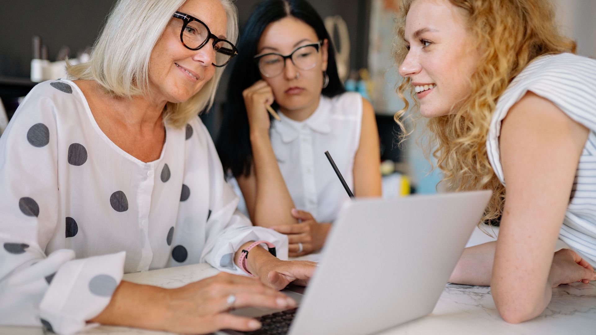 Three women collaborating at an office meeting around a laptop.