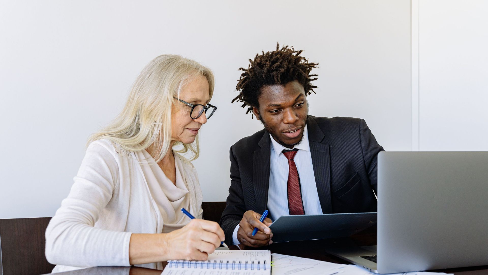 Two business professionals collaborating at a desk with laptops and documents in an office setting.