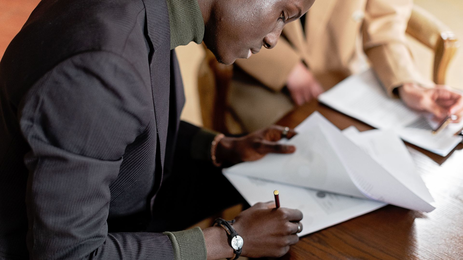 African American man focused on signing important business documents at a desk.