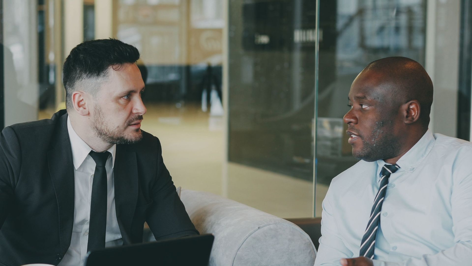 Two businessmen discussing at a cafe with a laptop and coffee.