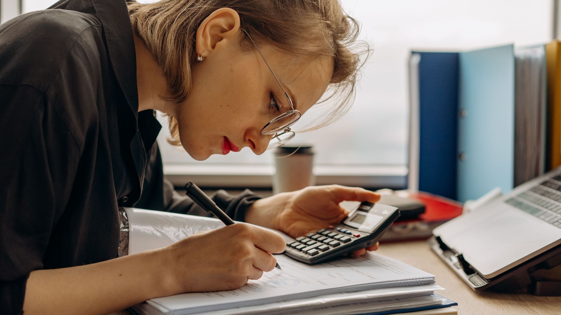 Young woman diligently working on accounting with a calculator and documents. Perfect for business and finance themes.