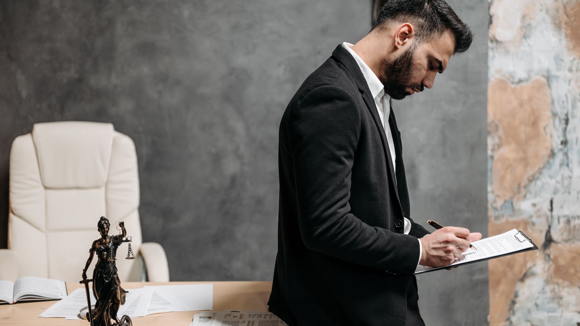 A lawyer in a black suit reviews paperwork at an office, focused and engaged.
