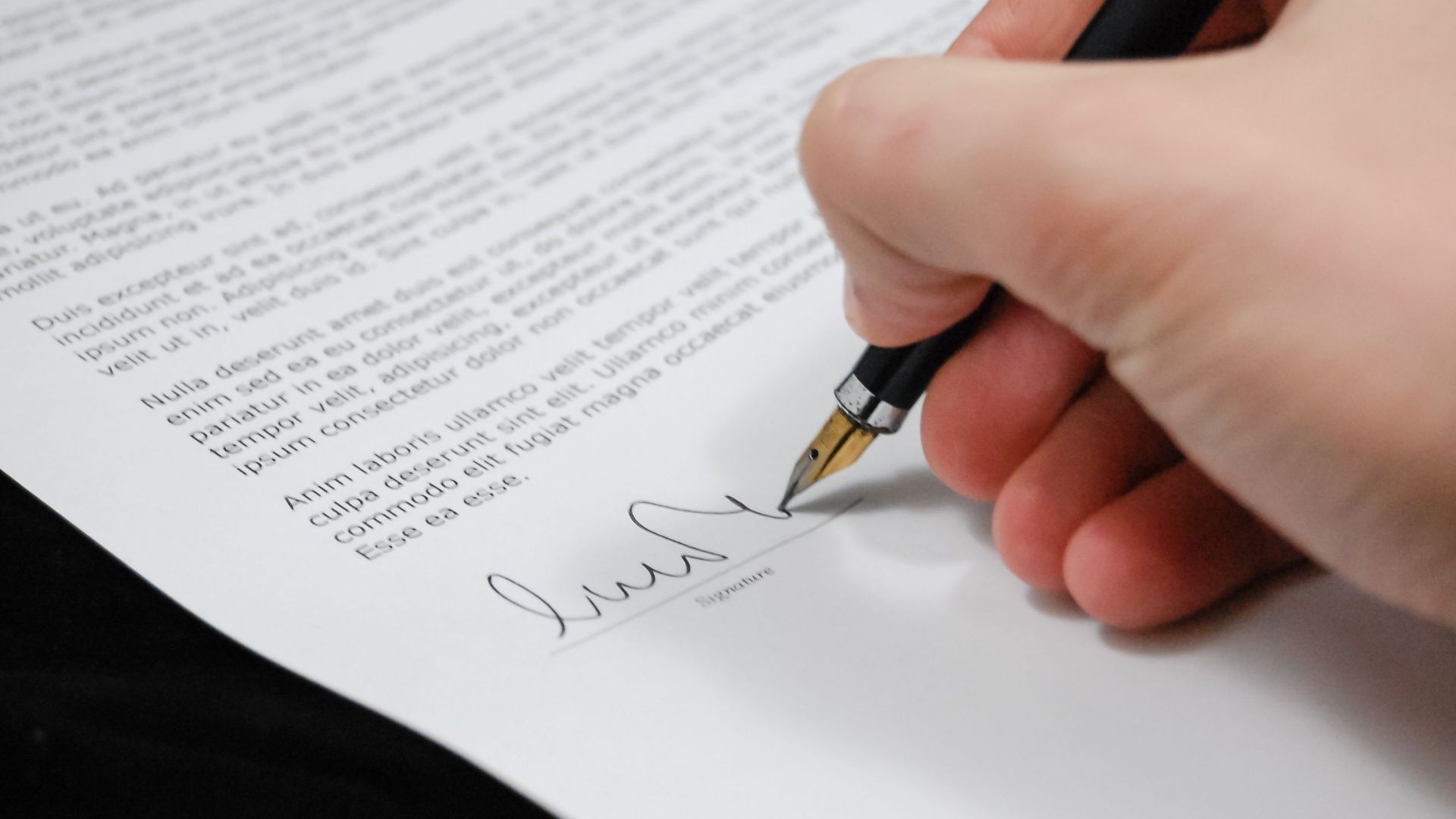 Close-up of a hand signing a legal document with a fountain pen, symbolizing signature and agreement.