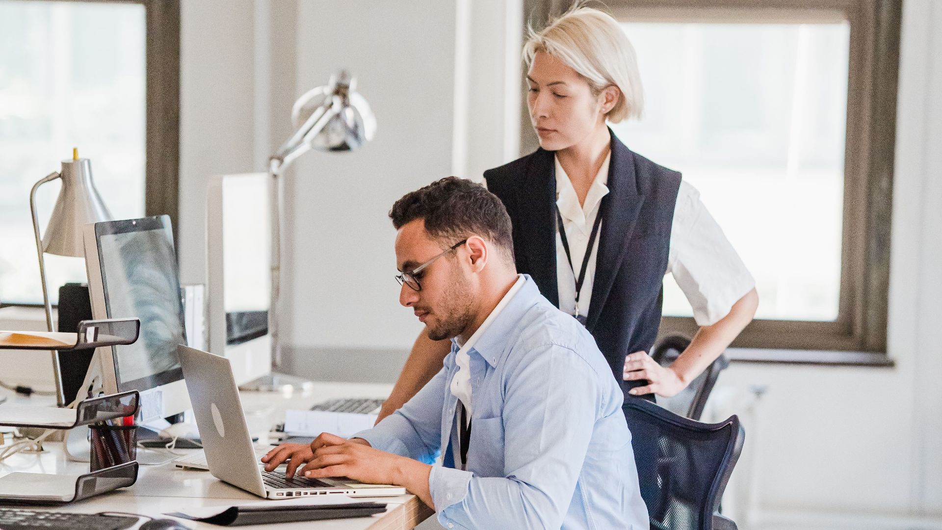 Two business professionals engaged in work at a modern office, using a laptop.