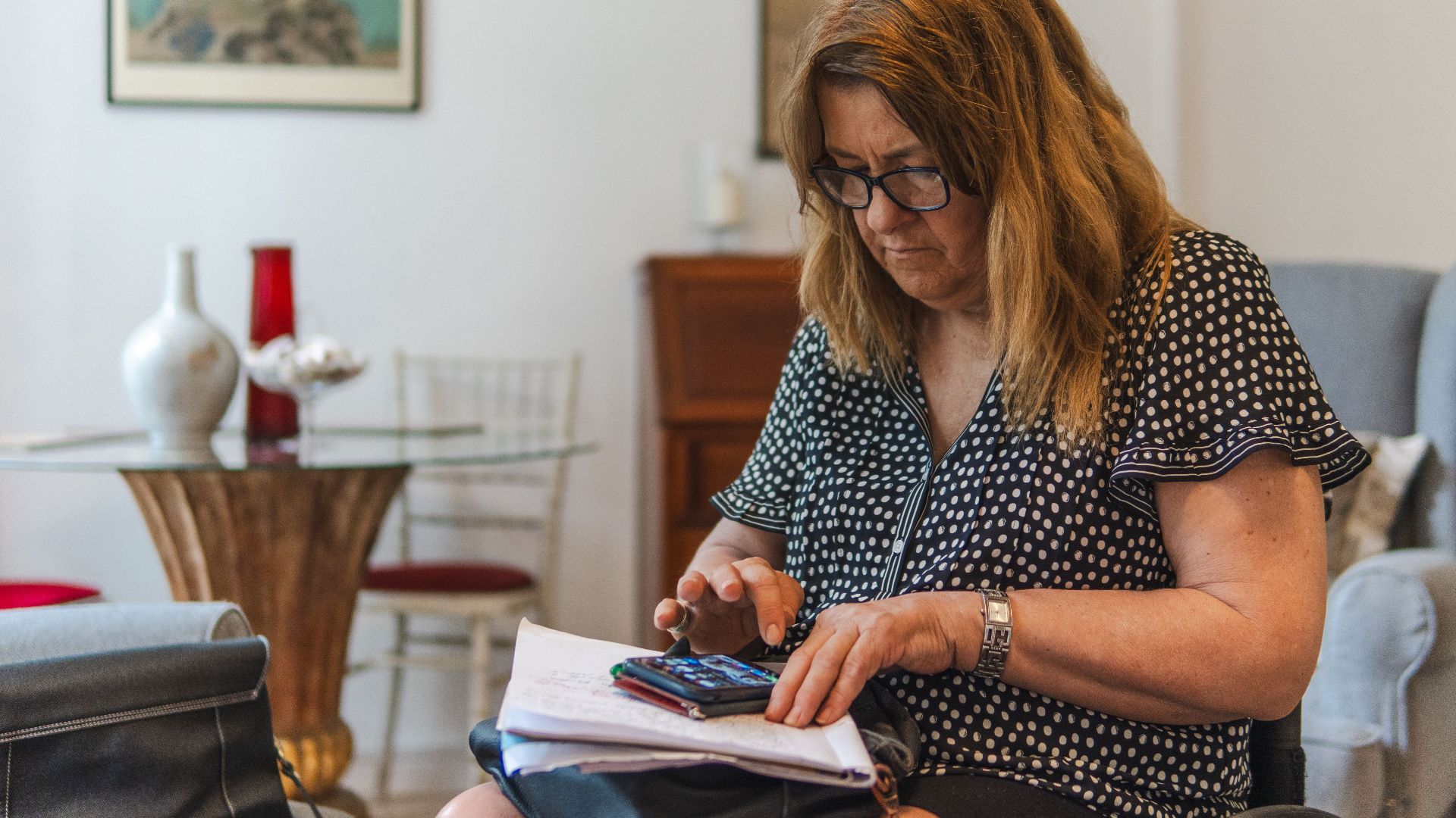 Focused woman calculating expenses with calculator and notebook at home.