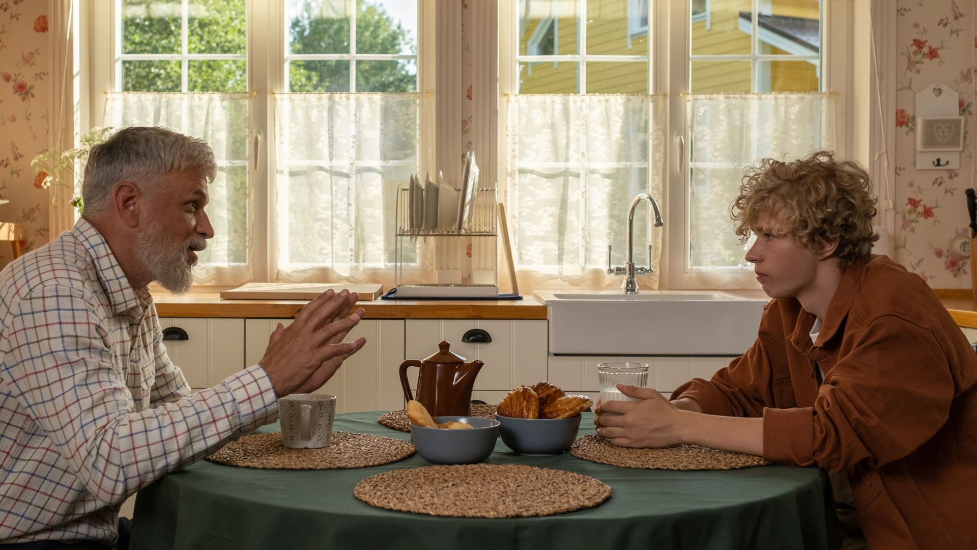 Elderly man and teenage boy enjoying breakfast and conversation at a table.