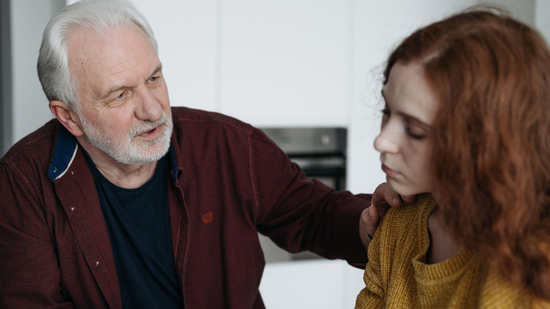 An elderly man consoles a young woman indoors, expressing empathy and understanding.