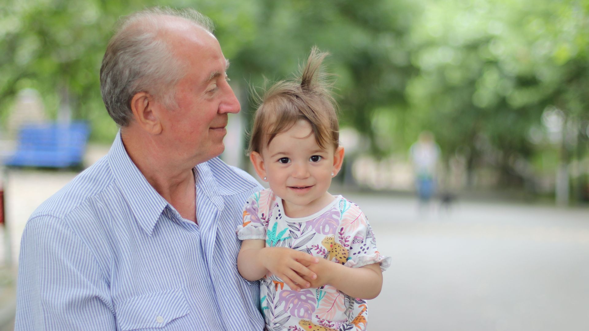 A joyful moment with a grandfather holding his grandchild in a sunny park.