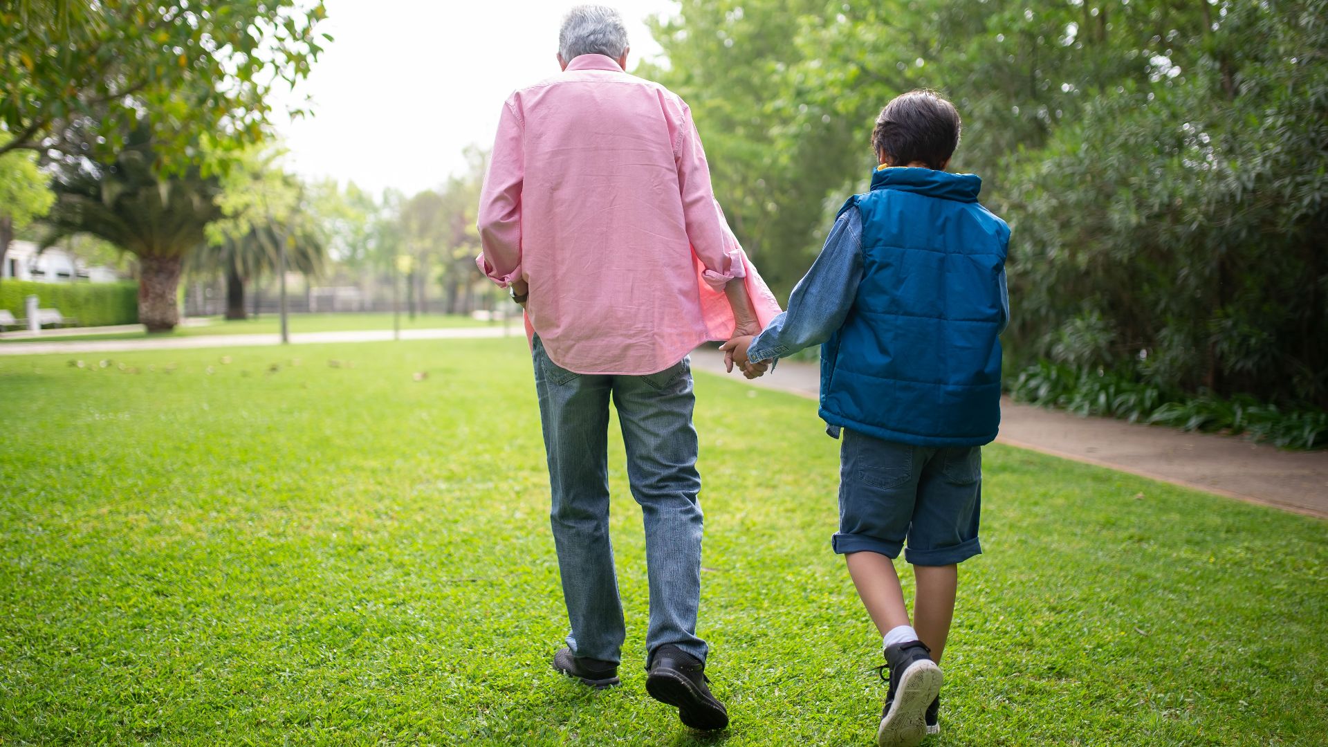 A grandfather and grandson walk hand in hand through a green park in Portugal.
