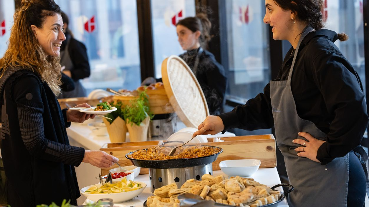 Smiling woman served at a buffet with various dishes by a friendly staff member.