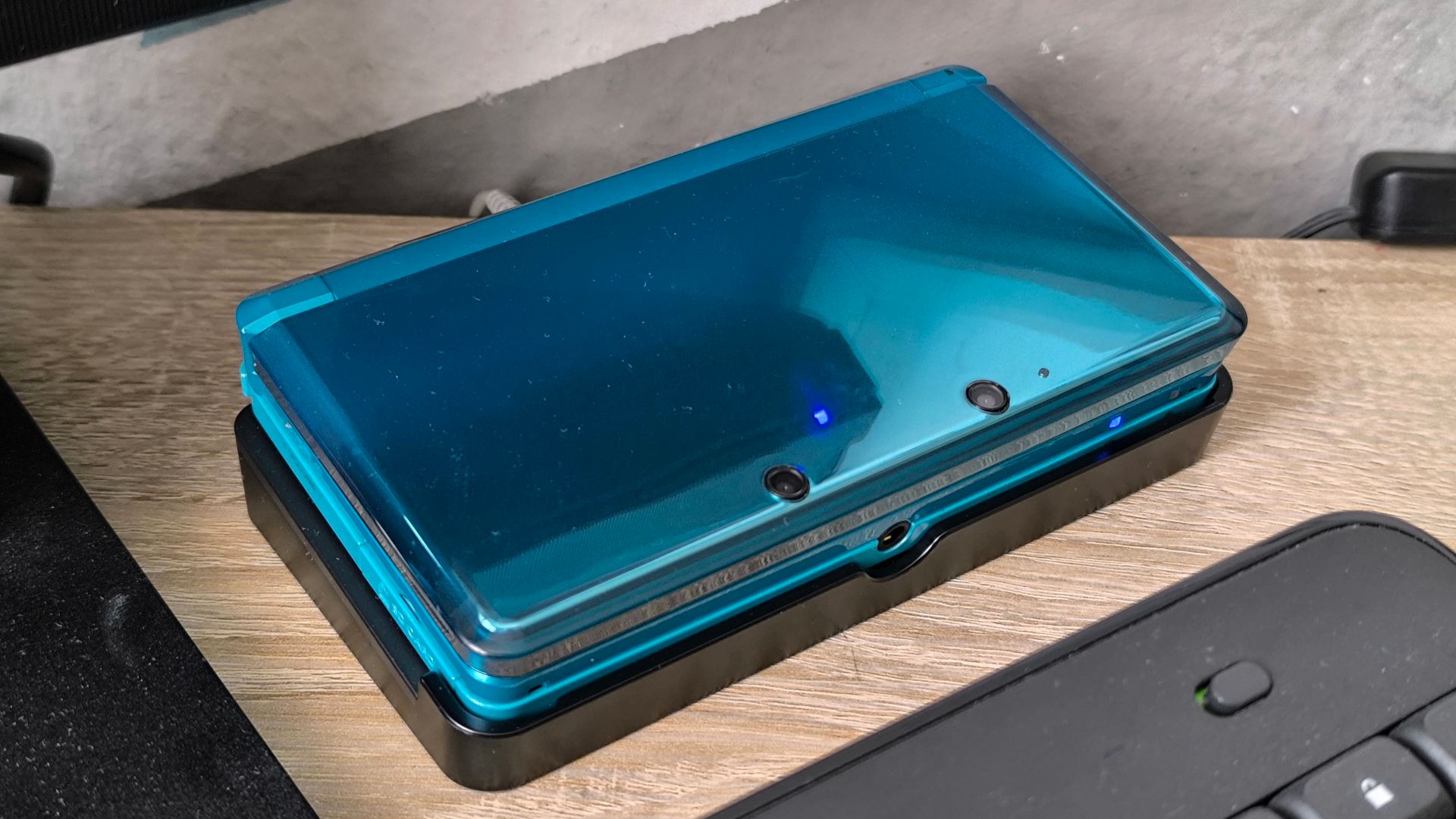 Nintendo 3DS in der Farbe Aqua Blau zugeklappt in der migelieferten Ladestation. Zu erkennen- Die beiden 3D-Außenkameras.