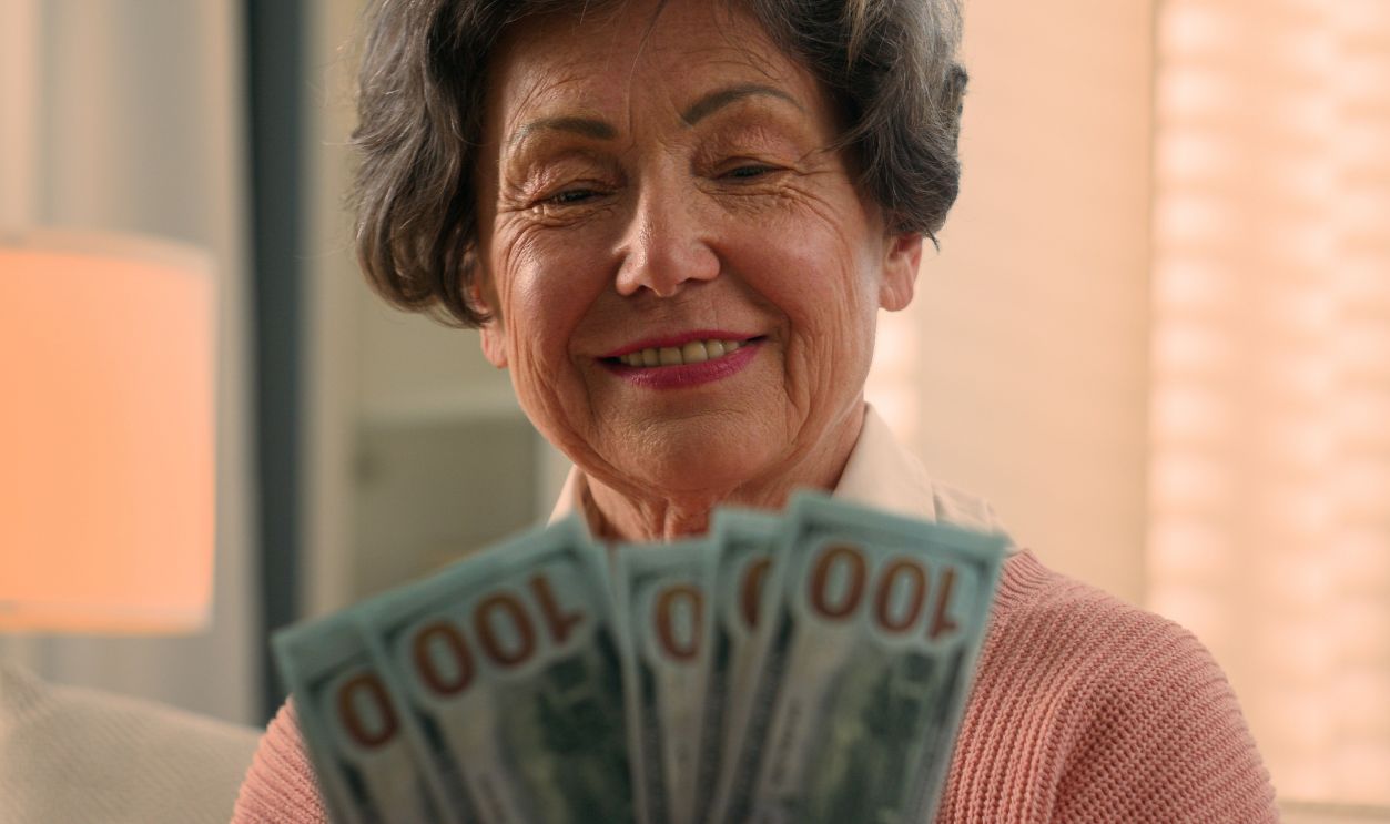 Happy smiling rich Caucasian old woman count money at home bills winning bonus grandmother counting dollars senior granny holding cash old female elderly retired lady with banknotes financial savings