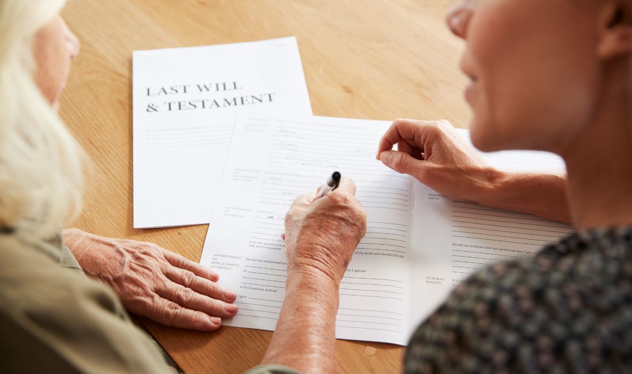 Female Friend Helping Senior Woman To Complete Last Will And Testament At Home
