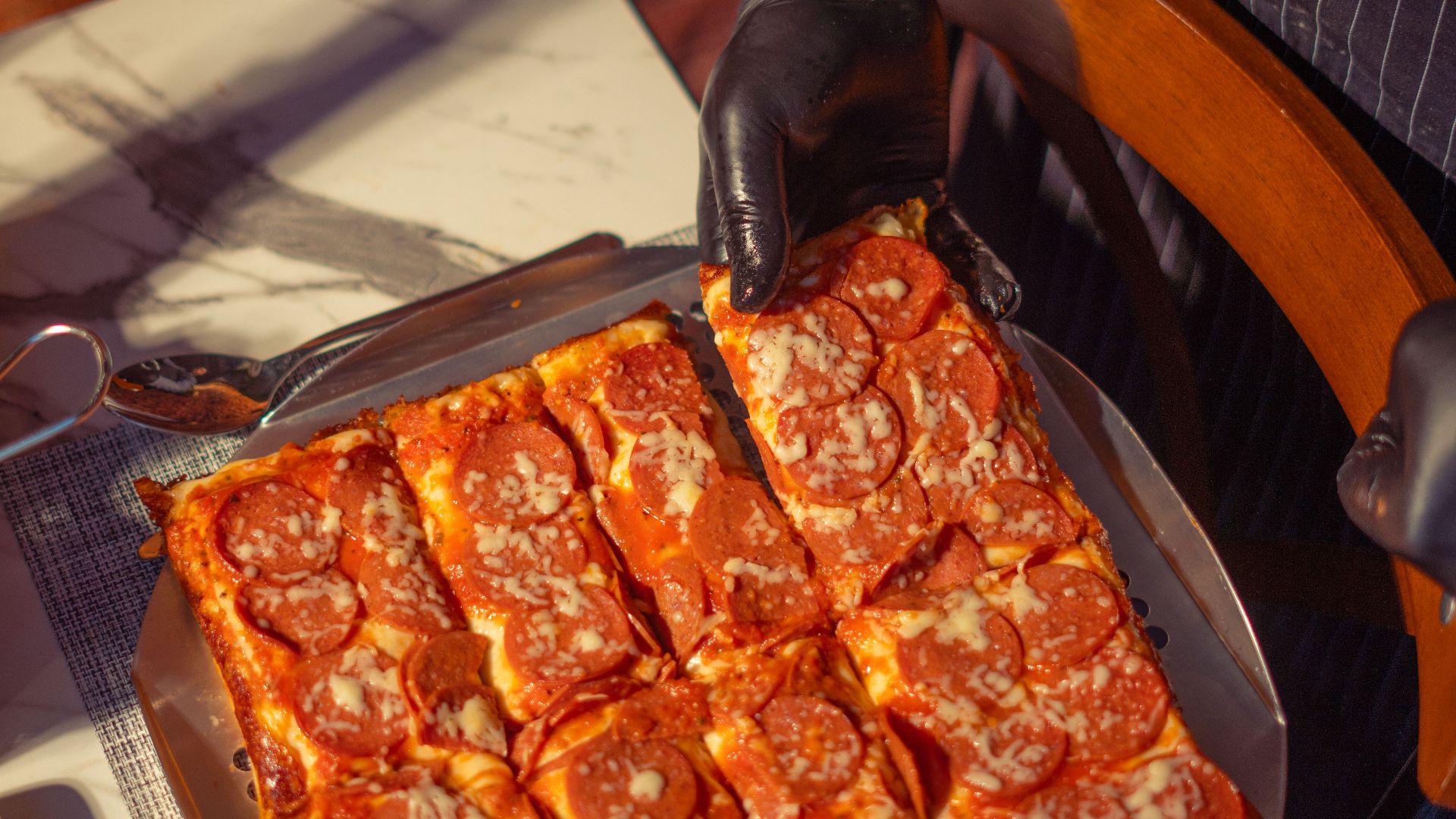 Delicious pepperoni pizza served on a tray with a gloved hand indoors.