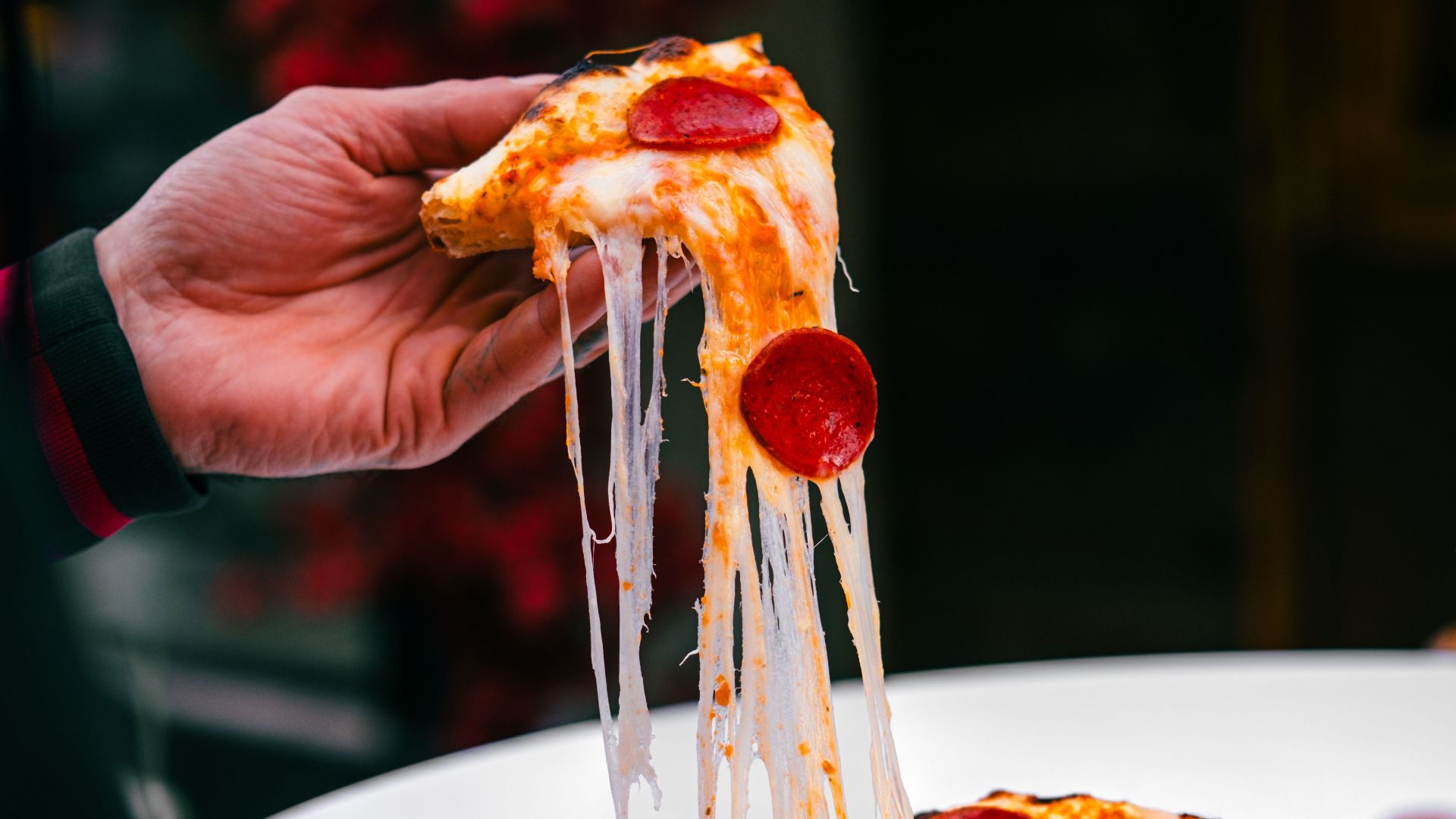 Close-up of a hand holding a pepperoni pizza slice with a gooey cheese pull, creating an appetizing scene.