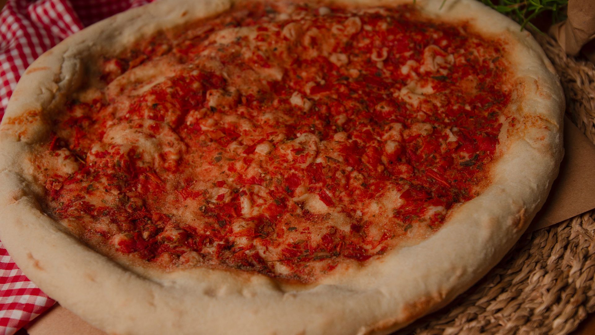 Close-up of a freshly baked cheese pizza with tomato sauce on rustic placemat.