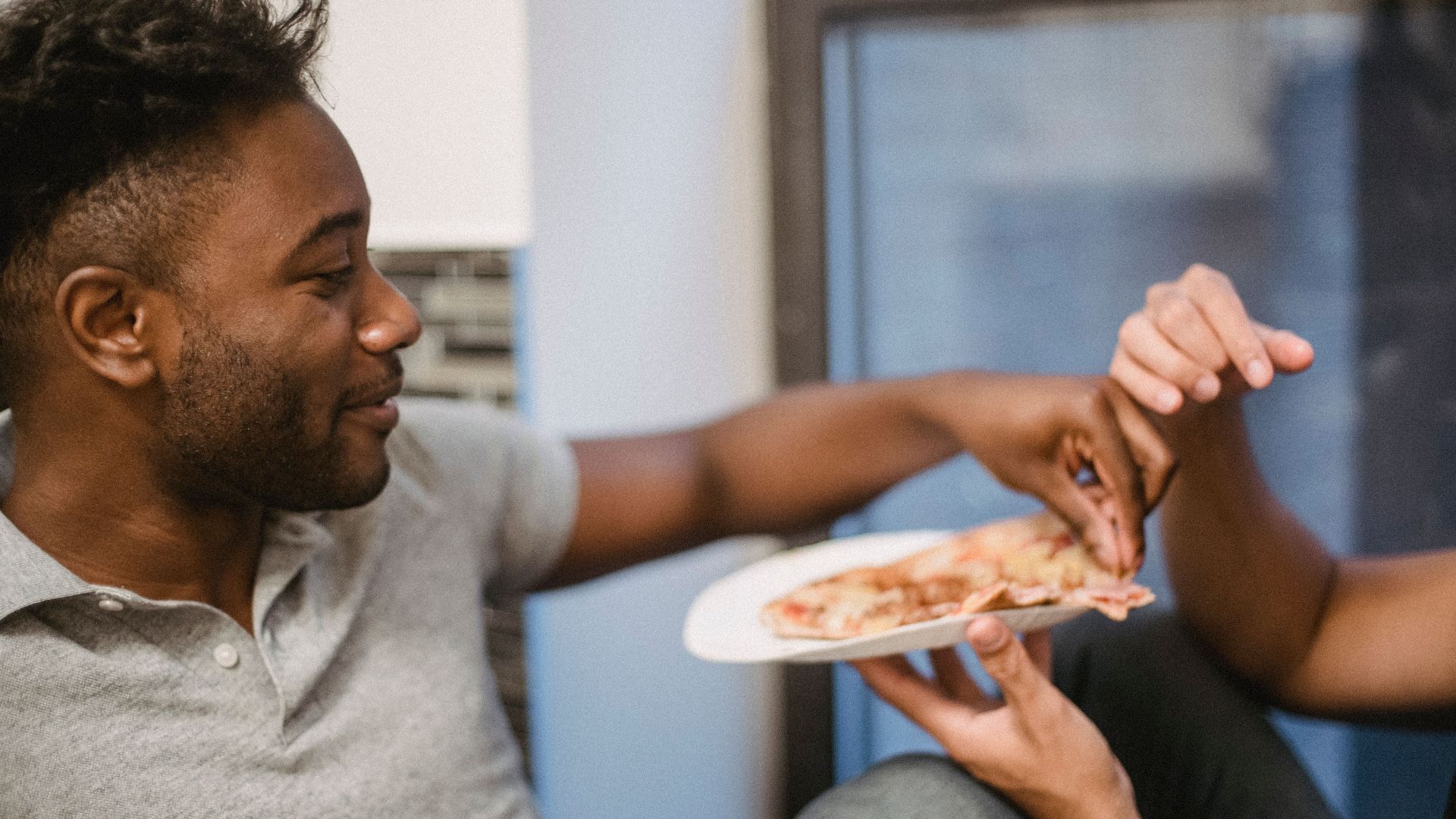 Close-up of friends sharing pizza indoors, adding a touch of laughter and warmth to the scene.