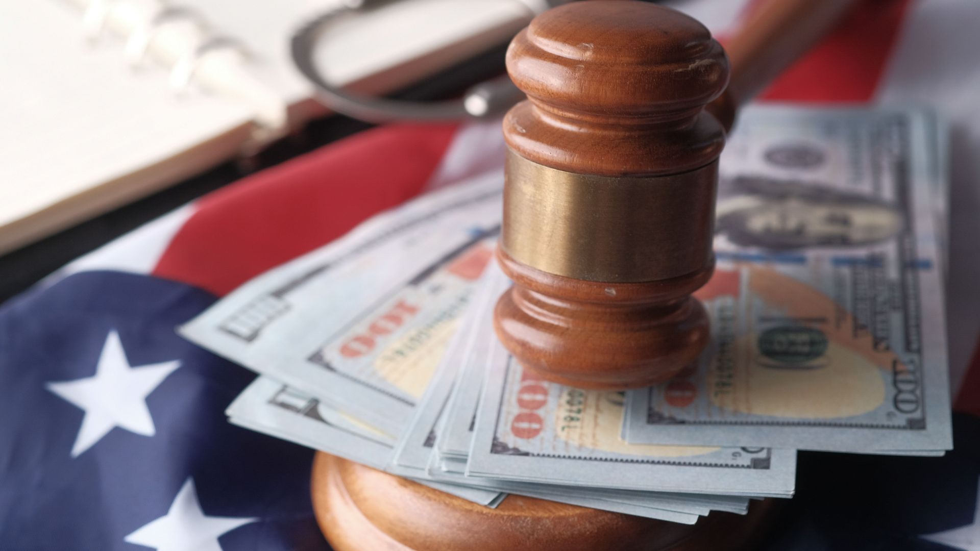 Close-up of a judge's gavel resting on US dollar bills and an American flag, symbolizing justice and finance.
