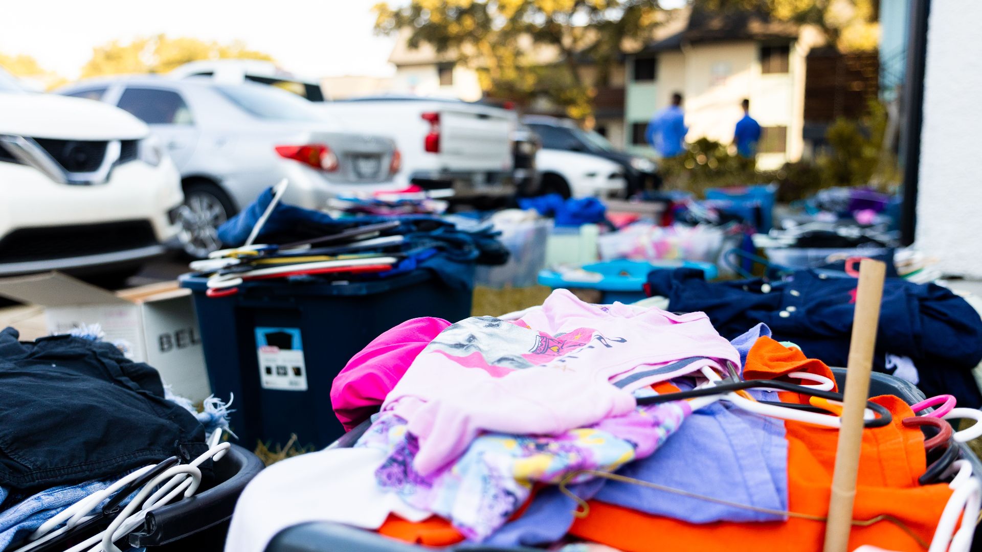 An outdoor garage sale featuring various clothes and cars in a suburban setting.