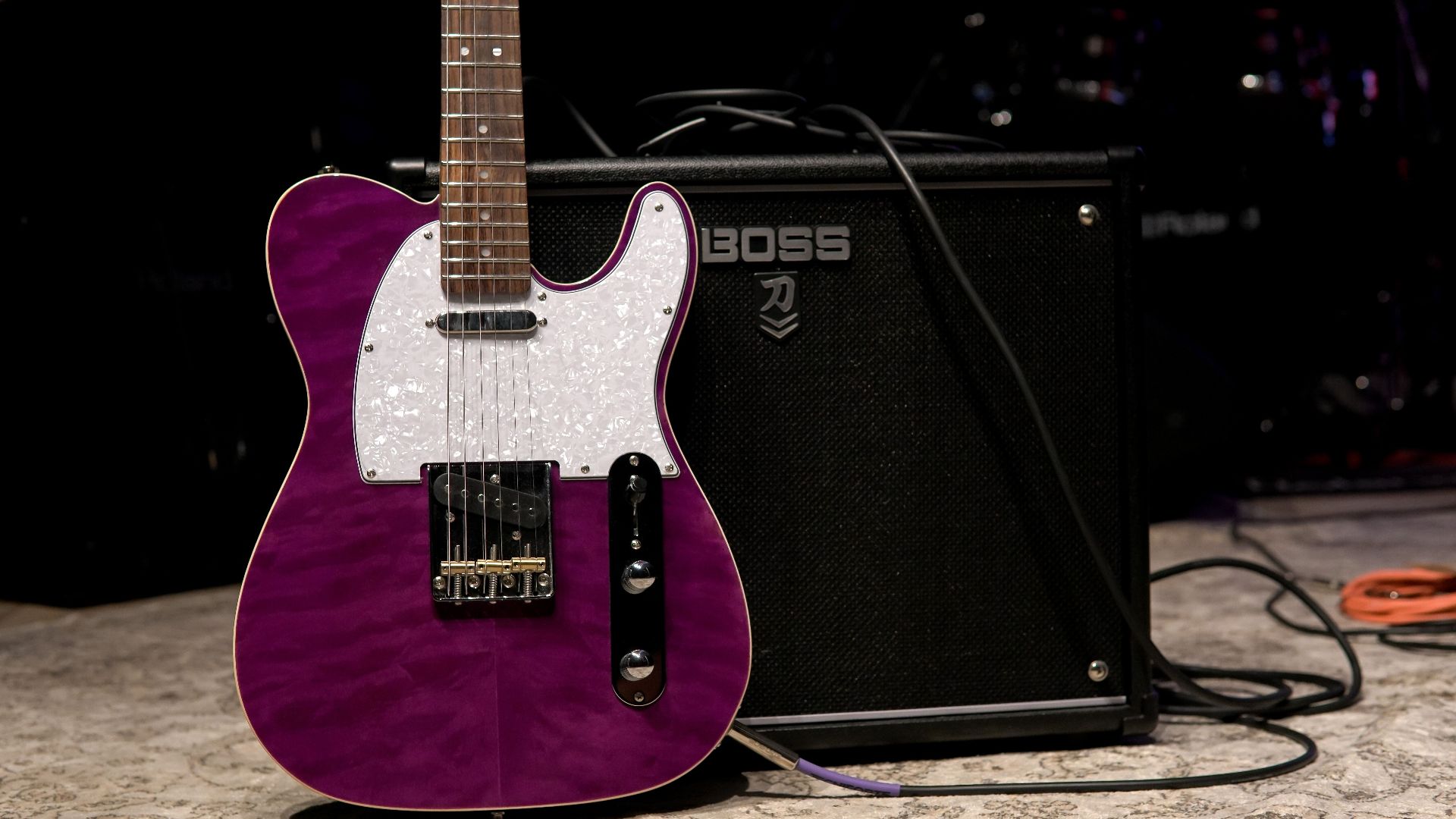 Vibrant purple electric guitar next to amplifier on stage, ready for a performance.