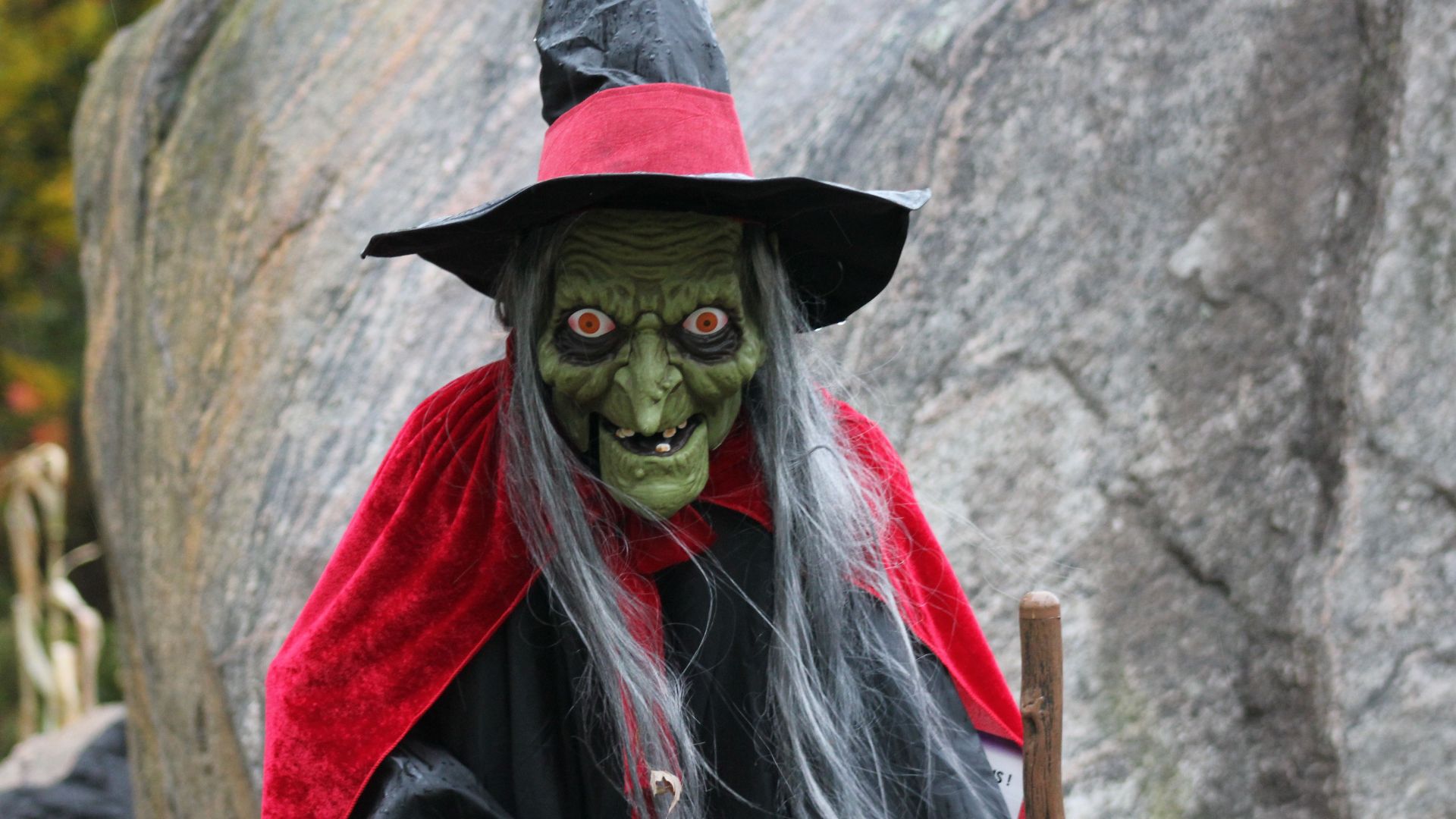 Scary witch with green face and black hat outdoors, perfect for Halloween themes.