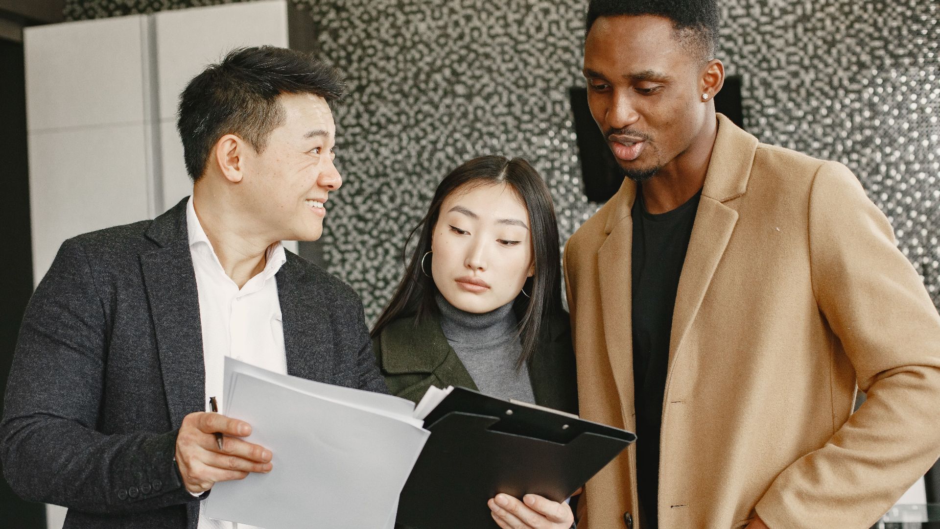 Three diverse professionals discussing a document indoors, showcasing teamwork and collaboration.