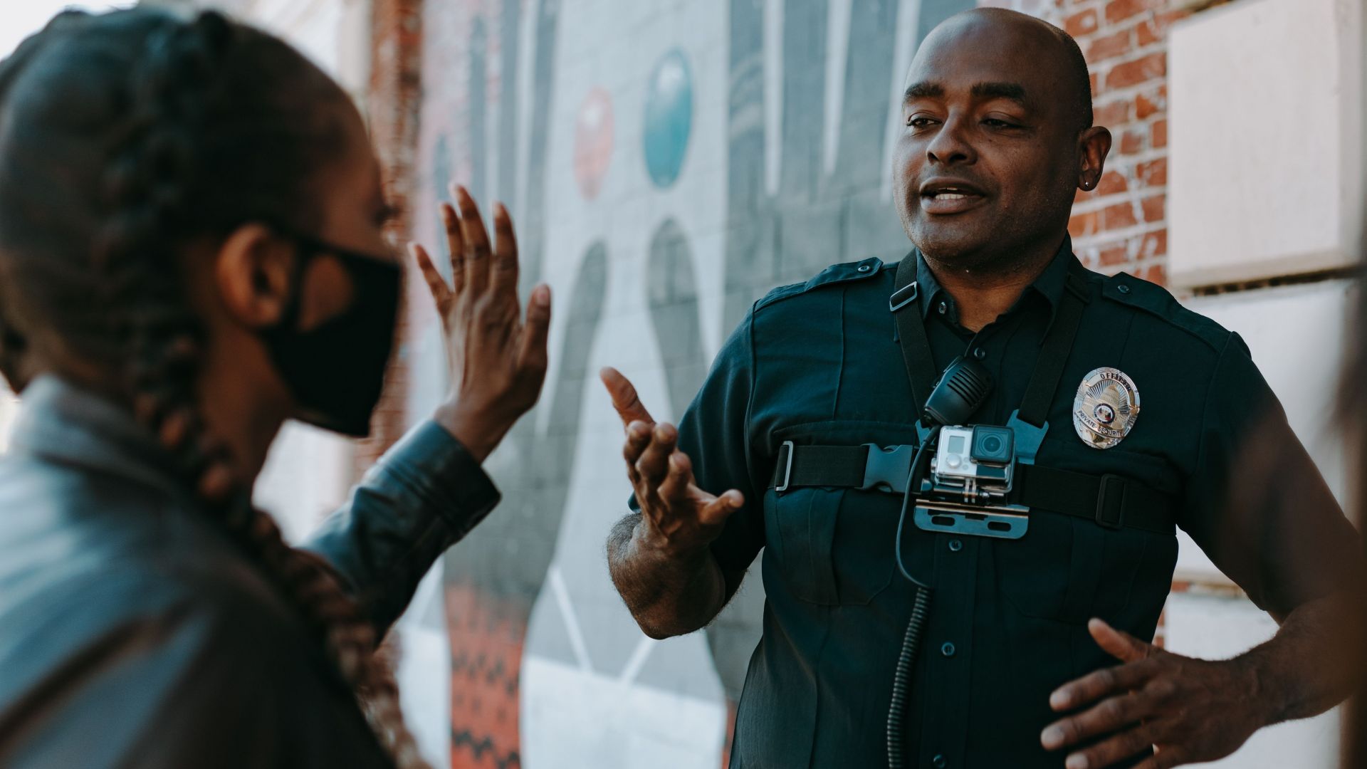 Police officer conversing with people on the street near a brick wall mural.