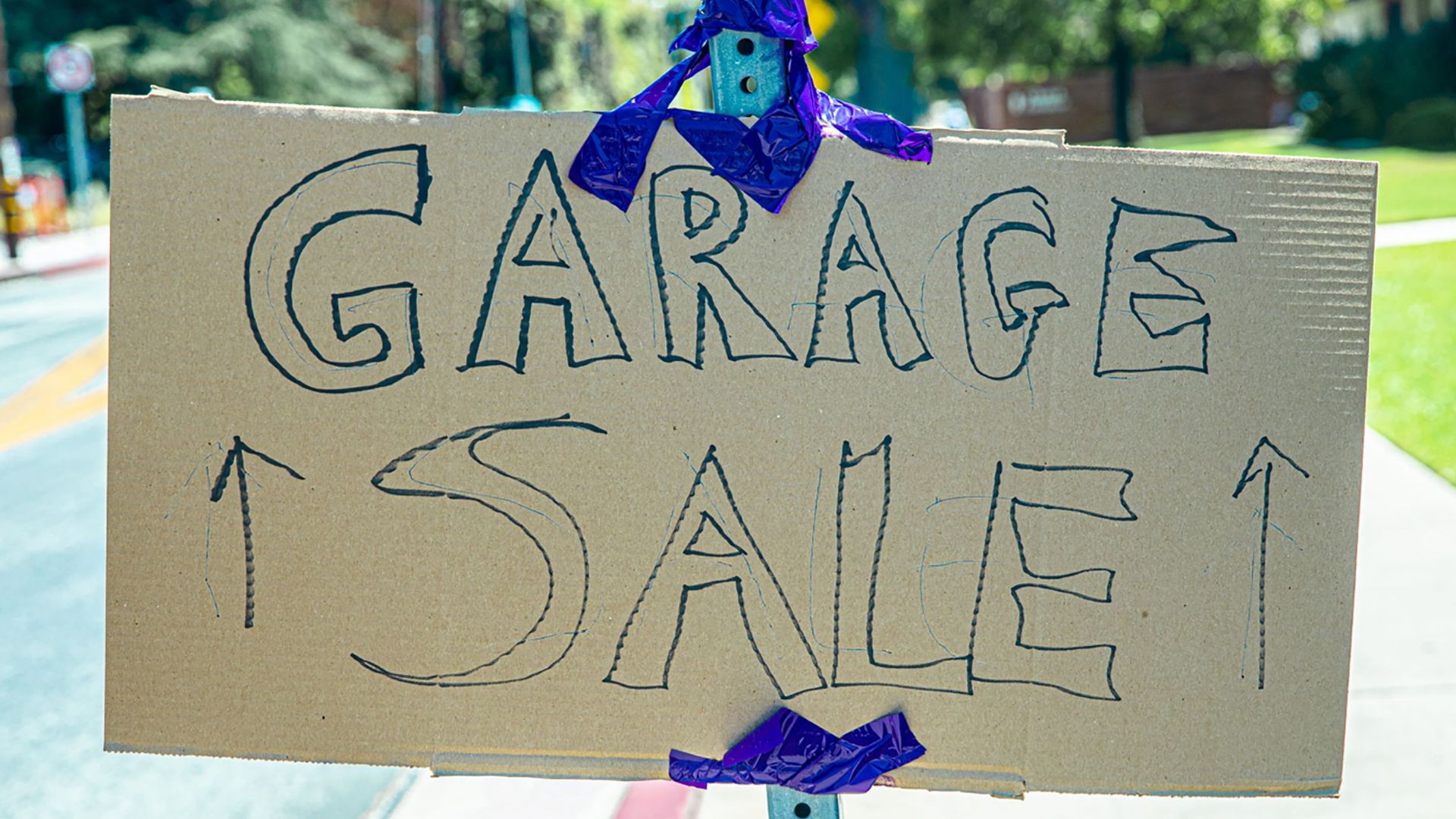 A handwritten garage sale sign taped on cardboard, displayed outdoors.