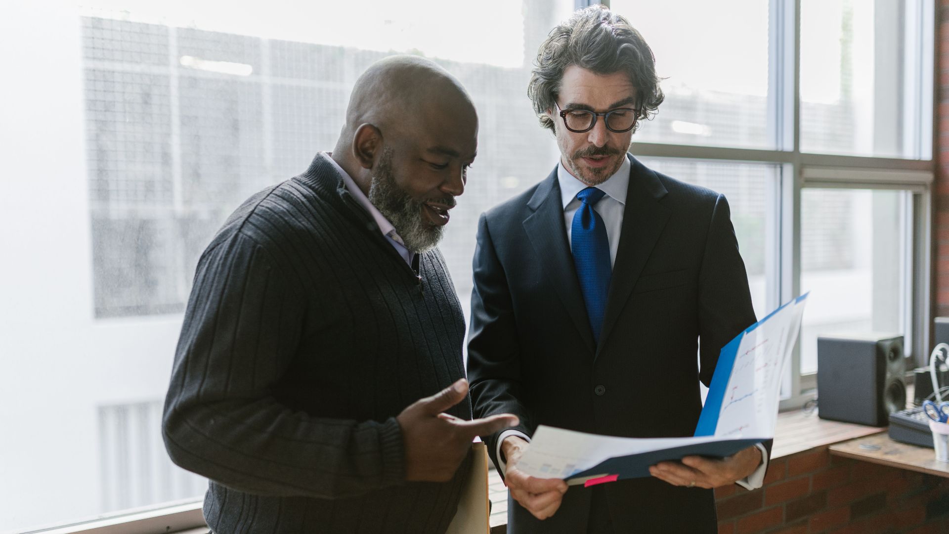Two businessmen discussing and reviewing documents in a modern office setting.