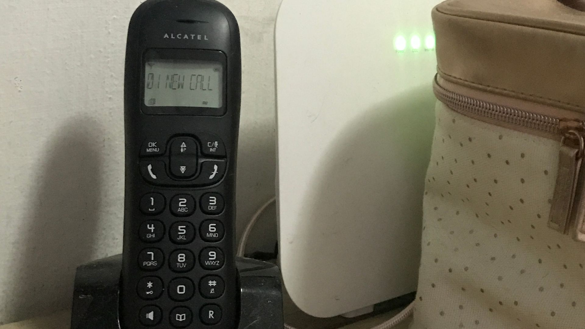 Black Alcatel Cordless phone beside modem