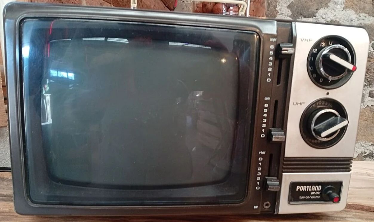 This television is an old, portable television that was used during the 1970s. It was a device that did not yet require a remote control to be used; its use was solely to display images transmitted in black and white.