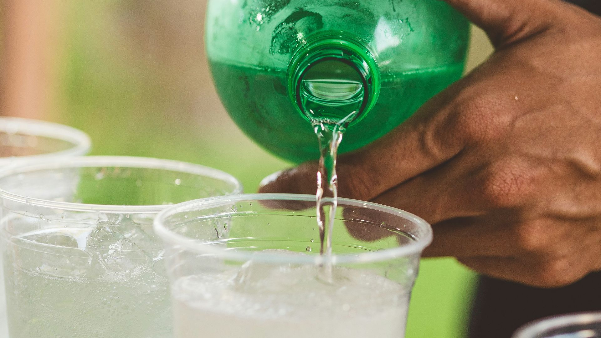 Hand pours drink from green bottle into plastic cup