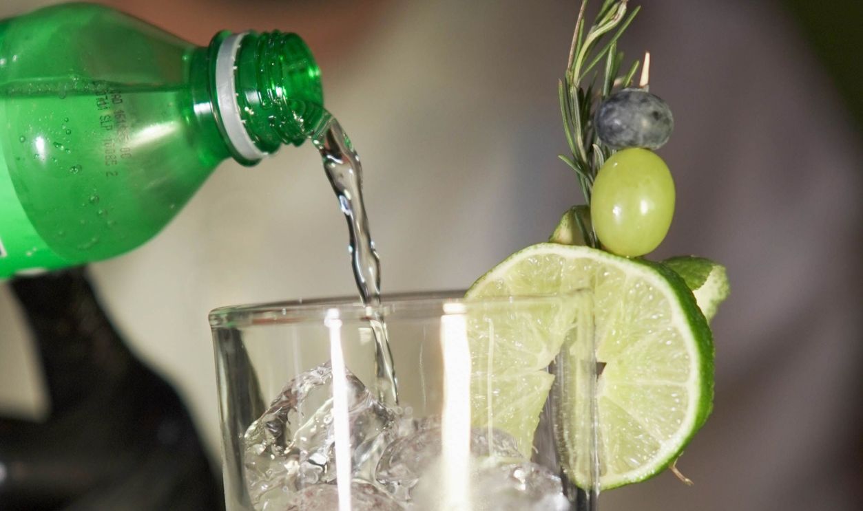 A barman creating a craft cocktail with lime, rosemary, and berries, adding soda