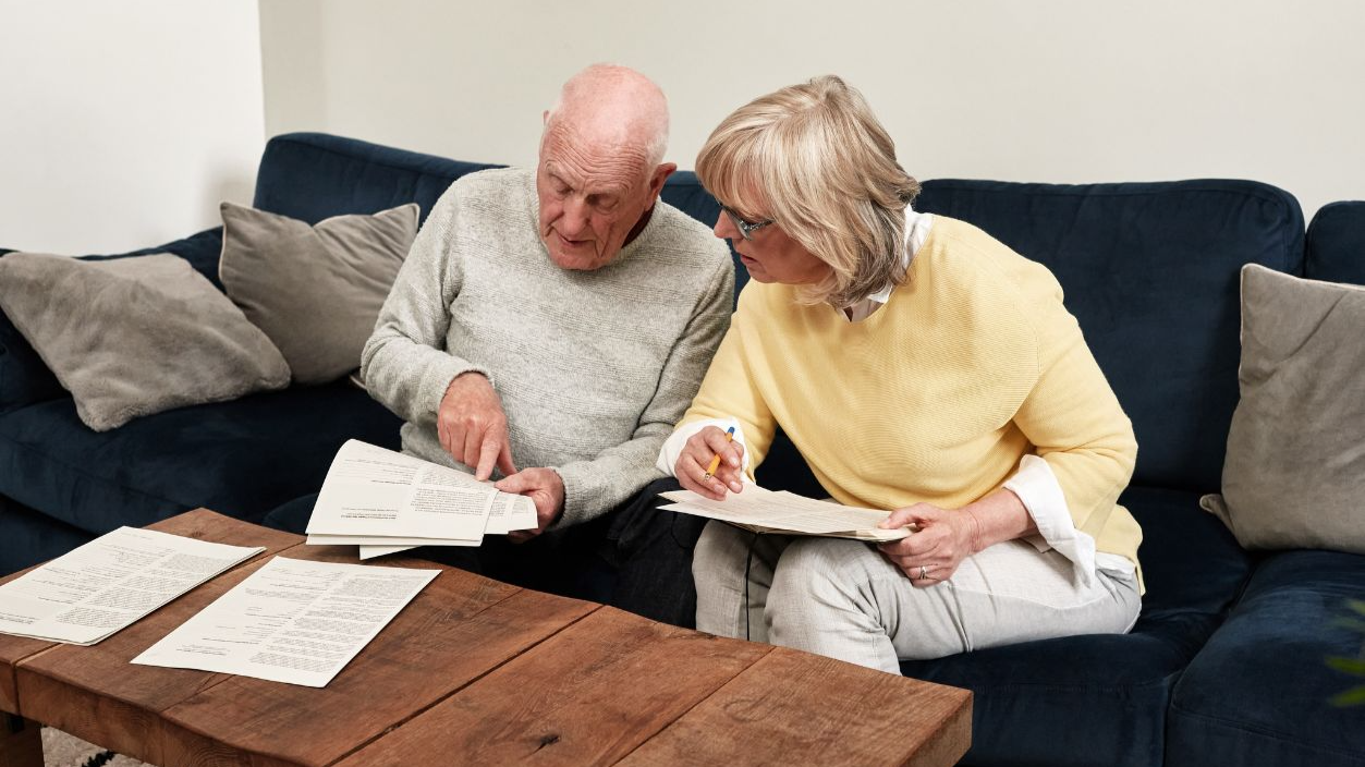 Shutterstock-2620575113, Senior couple reading documents in home for planning budget, financial assets and legal contract for insurance policy. Man, woman and paperwork of investment information, bills and retirement savings
