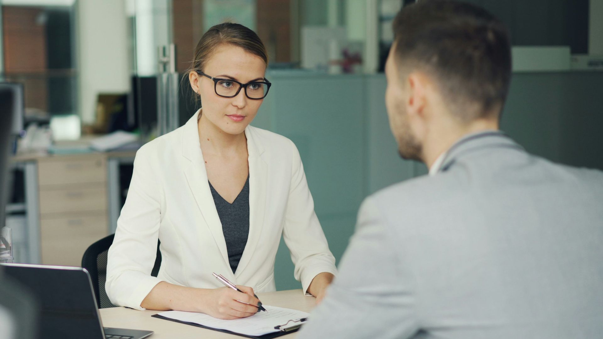 Woman in glasses interviews man at office desk