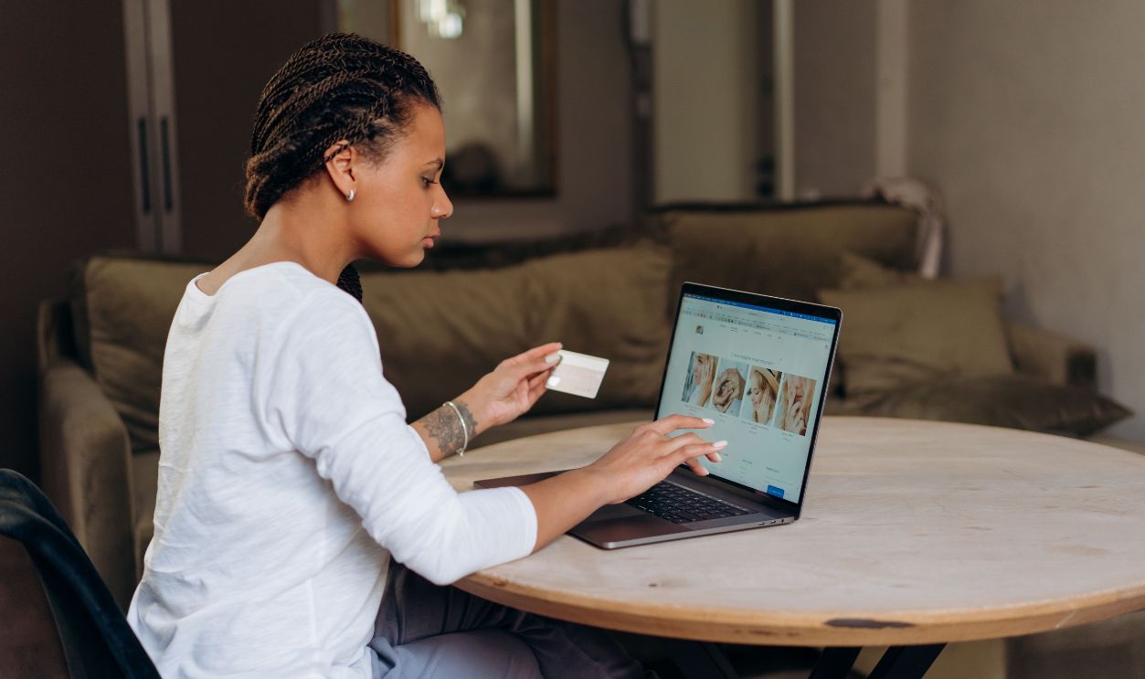 African American woman uses a credit card for an online purchase on her laptop at home.