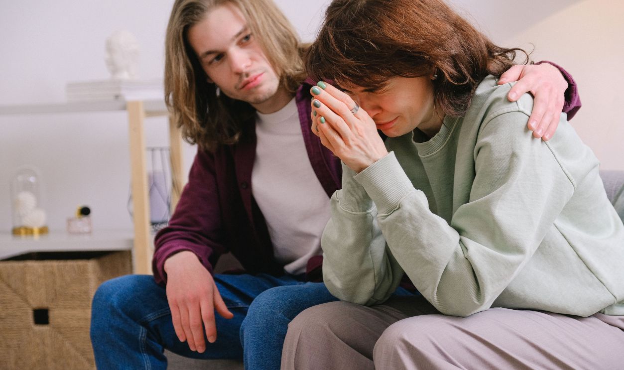 A man comforts a crying woman indoors, conveying support and understanding in a difficult moment.