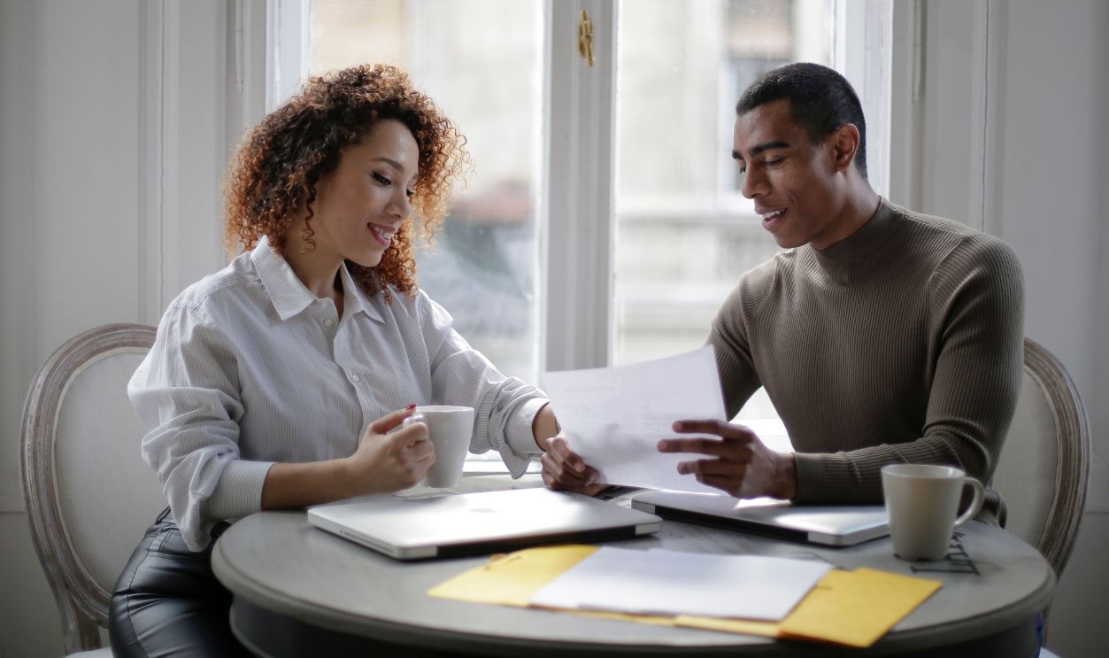 Two colleagues discussing business documents over coffee in a bright office setting.