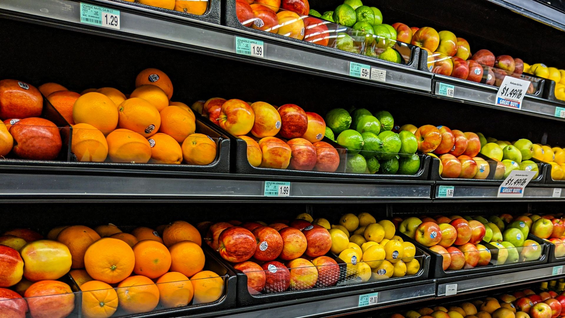 Shelves of fresh oranges, apples, lemons, and limes in a grocery store