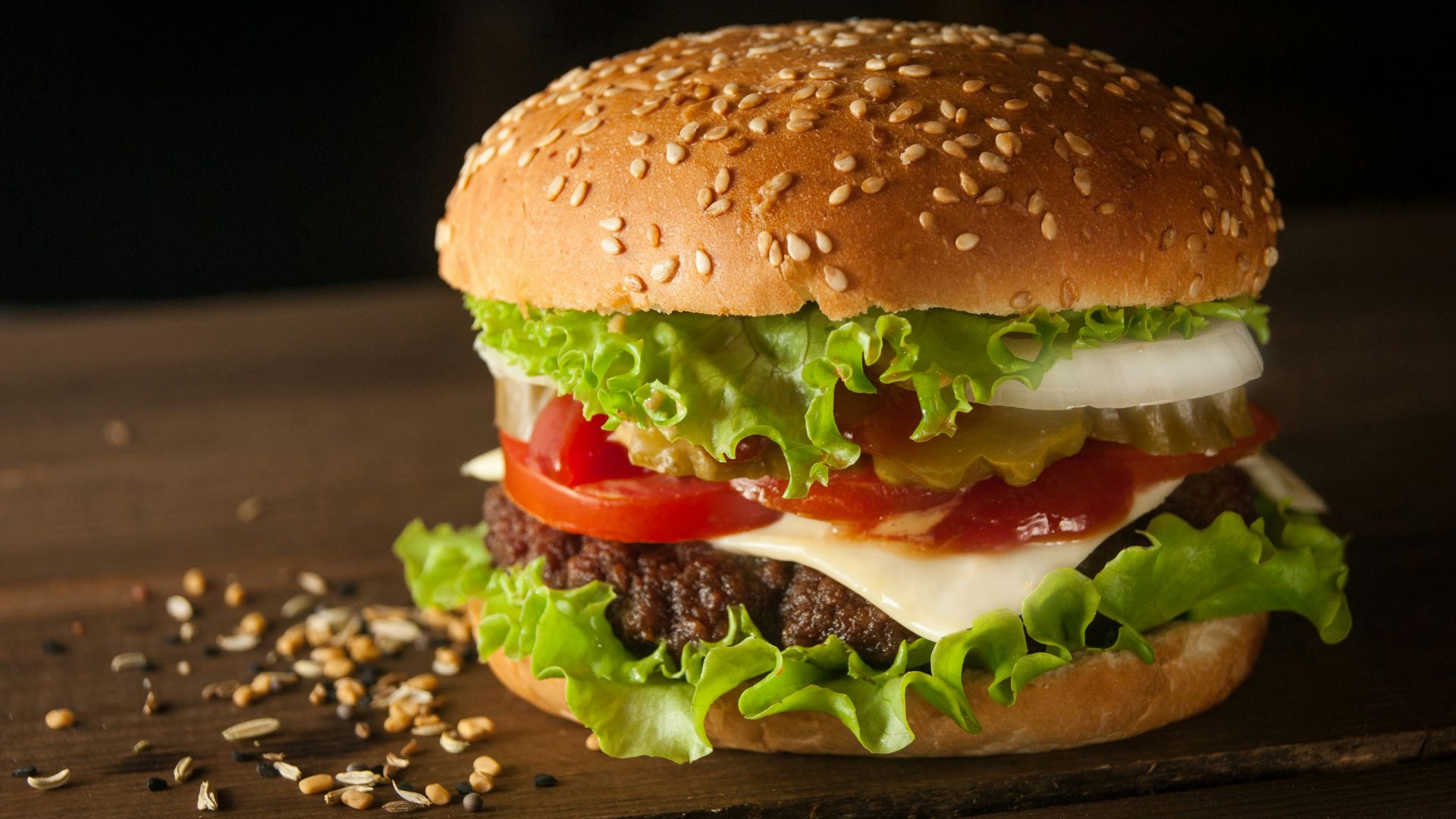 A cheeseburger with lettuce, tomato, and onion on a dark wooden surface